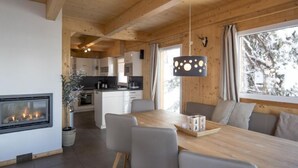 Une cuisine moderne avec des meubles blancs, un îlot central et un coin repas comprenant une table en bois et des chaises grises.