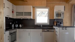 Une cuisine compacte avec des meubles blancs, un plan de travail noir, un four encastré, un lave-vaisselle et un four à micro-ondes.