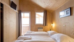 Une chambre de style cabane en bois, avec deux lits, une fenêtre avec des rideaux, un téléviseur fixé au mur et un tableau encadré accroché au mur.
