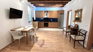 Eine kompakte Küche mit Holzschränken, einer schwarzen Arbeitsplatte und einem eingebauten Backofen. Es gibt eine Essecke mit einem Holztisch und weißen Stühlen.