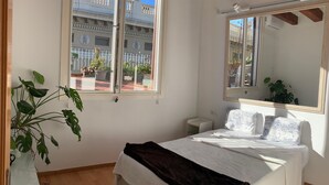 Ein Schlafzimmer mit einem Bett, einem großen Fenster, einem Spiegel und einer Zimmerpflanze.