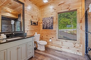 Baño de cabaña de madera con lavamanos, inodoro y ventana con vista a follaje.