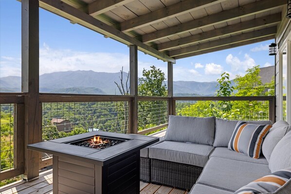 A covered outdoor seating area with a fire feature, overlooking a mountainous landscape.