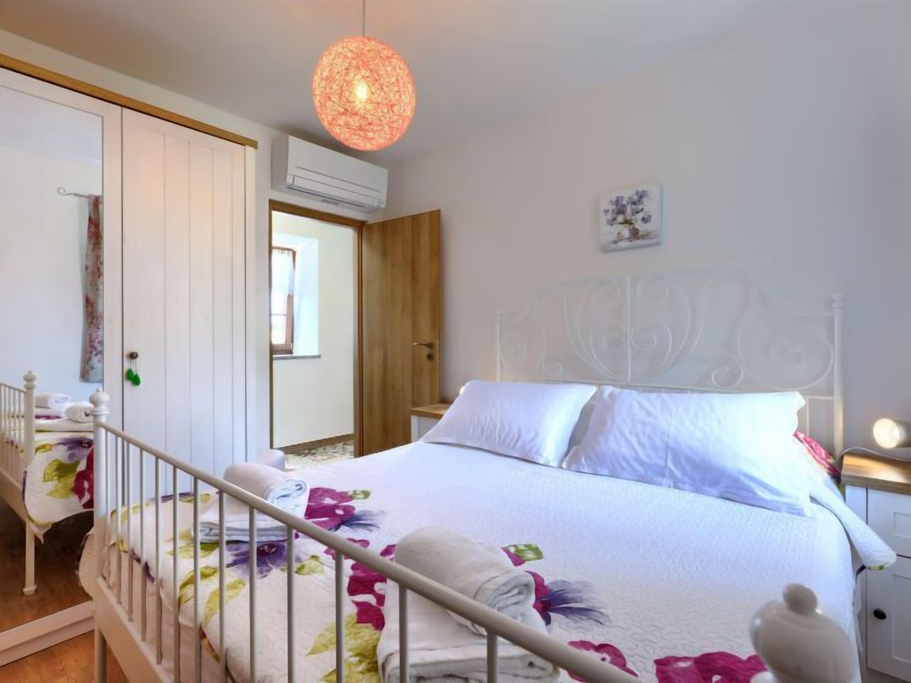 A bedroom with a bed, a white headboard, a hanging light fixture, and a door leading to another room.