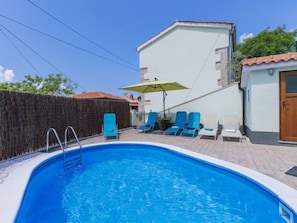 A swimming pool with a ladder, surrounded by blue lounge chairs and a yellow umbrella.