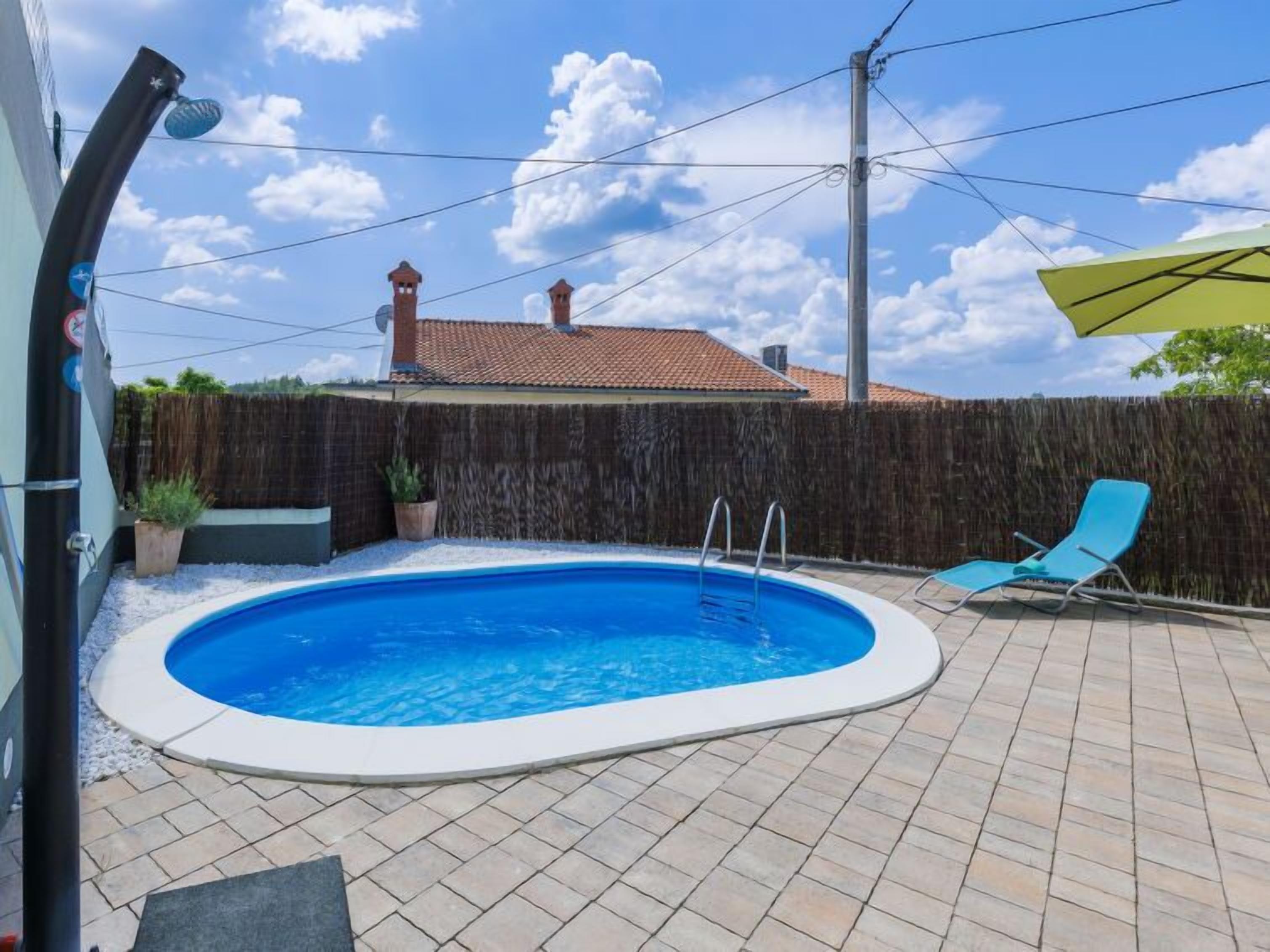 A backyard with a swimming pool, a wooden fence, and a blue lounge chair.