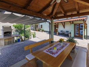 An outdoor patio with a wooden table, benches, and a barbecue grill.