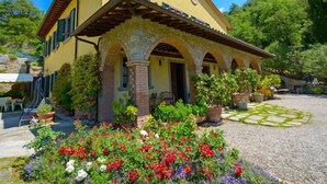 A yellow villa with a tiled roof, stone arches, and a garden with colorful flowers. - Il Farinaio by Interhome (Cortona)