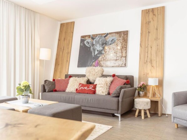 Ein modernes Wohnzimmer mit grauem Sofa, roten und weißen Kissen, einer Holzvertäfelung an der Wand und einem gerahmten Kunstwerk über dem Sofa.
