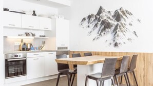 Una cocina moderna con armarios blancos, una mesa de comedor de madera y una gran obra de arte con motivos de montaña en la pared.