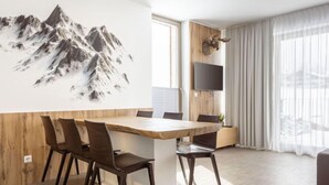 Un comedor moderno con una mesa y sillas de madera, una obra de arte de montañas en la pared, una cabeza de ciervo montada y un televisor en la pared.