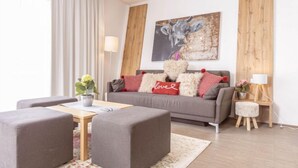 Una sala moderna con un sofá gris, dos otomanes grises, una mesa de centro de madera y un tapete floral.