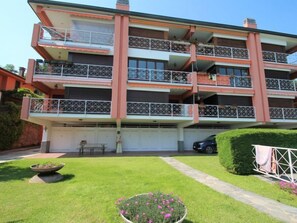 A multi-story building with balconies, a covered parking area, and a well-maintained lawn with flower beds. - Casa sul lago di Lea by Interhome (Monvalle)