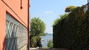 A stone-paved patio with a view of a lake, a red building with a window, and a hedge.