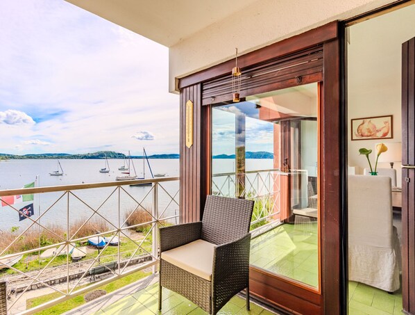 A balcony with a wicker chair, a glass door leading to a room, and a view of boats on a lake. - Casa sul lago di Lea by Interhome (Monvalle)