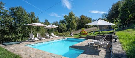 A swimming pool with lounge chairs and umbrellas, surrounded by a stone deck and greenery.