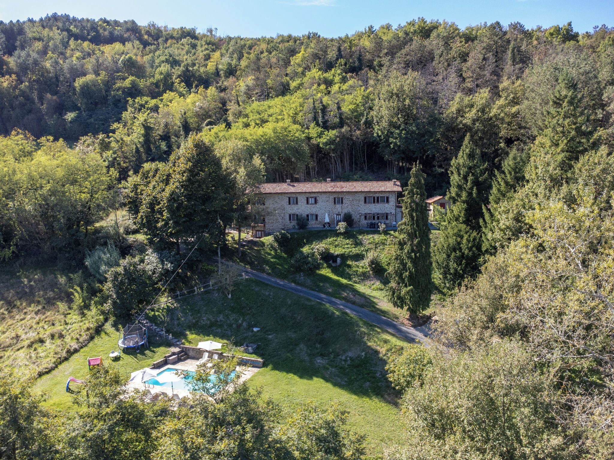 A stone house with a swimming pool surrounded by lush greenery and trees.