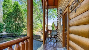 A wooden cabin with a porch, a rocking chair, and a view of a forested area. - A Bliss - game room, pool access, hot tub and more (Sevierville)