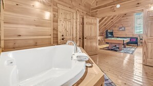A wooden cabin interior with a large white bathtub, wooden floors, and a cozy living area with a pool table. - A Bliss - game room, pool access, hot tub and more (Sevierville)