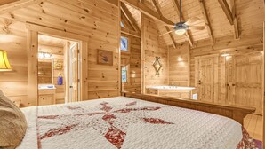 A wooden cabin room with a bed, a ceiling fan, a bathroom with a sink, and wooden walls. - A Bliss - game room, pool access, hot tub and more (Sevierville)