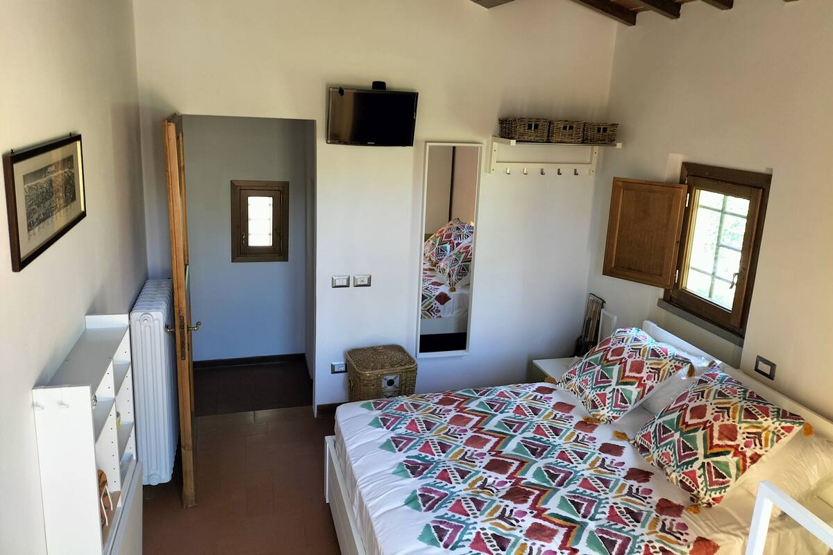 A bedroom with a bed, a television, a window, and a door leading to another room.
