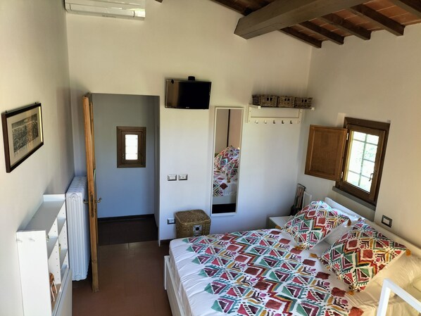 Un dormitorio con una cama, un televisor, una ventana y una puerta que da a otra habitación.