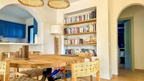 A dining area with a wooden table and chairs, a bookshelf with books, and a kitchen visible through an archway. - Mediterranean Villa 900m from the beach! (Pals)