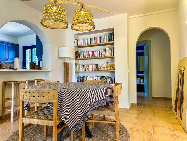 A dining area with a checkered tablecloth, wicker chairs, and a bookshelf filled with books. - Mediterranean Villa 900m from the beach! (Pals)