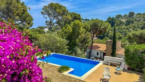 A swimming pool with a wooden deck and lounge chairs, surrounded by lush greenery and trees. - Mediterranean Villa 900m from the beach! (Pals)