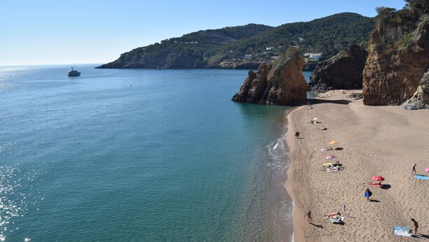 A beach with clear blue water, rocky cliffs, and a few people relaxing on the sand. - Mediterranean Villa 900m from the beach! (Pals)