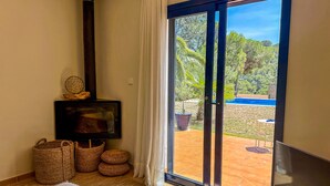 A room with a fireplace, wicker baskets, a sofa, and a sliding glass door leading to an outdoor area with a pool. - Mediterranean Villa 900m from the beach! (Pals)