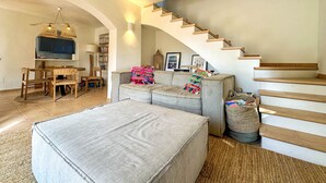 A spacious living room with a staircase, a dining area with wooden furniture, and a cozy seating area with a colorful blanket. - Mediterranean Villa 900m from the beach! (Pals)