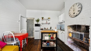 A compact kitchen with white walls, a wooden dining table, and a large clock. - Olive Nook in Katoomba (Katoomba)