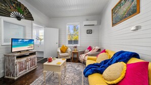 A cozy living room with a television, a sofa with colorful cushions, a small table, and a decorative fan. - Olive Nook in Katoomba (Katoomba)