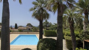 Une piscine entourée de palmiers et de haies bien entretenues.