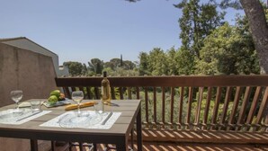 Un espace de restauration en plein air avec une table dressée pour deux personnes, une bouteille de vin et une assiette de nourriture.