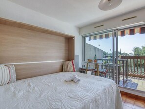 A hotel room with a large bed, a wooden headboard, a balcony with a table and chairs, and a view of the outdoors. - Le Bali by Interhome (La Ciotat)