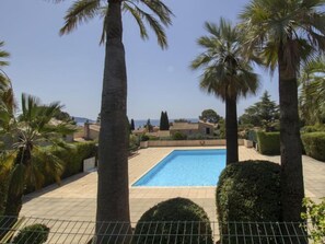 A rectangular swimming pool surrounded by palm trees and hedges, with a view of houses and the sea in the background. - Le Bali by Interhome (La Ciotat)