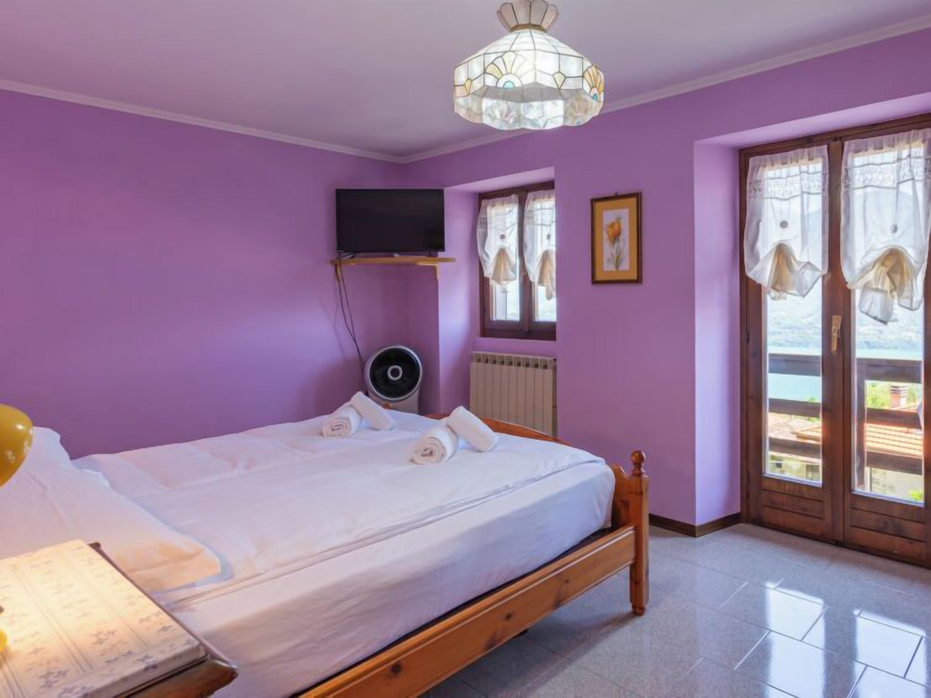 Une chambre à coucher avec un lit, un téléviseur fixé au mur, un radiateur et une fenêtre avec des rideaux.