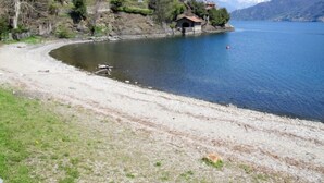 Vista del lago con un pequeño edificio en la orilla, rodeado de árboles y montañas al fondo.