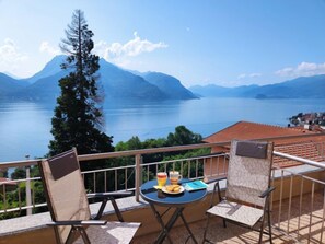 Ein Balkon mit Tisch für zwei Personen, mit Blick auf einen See und Berge.