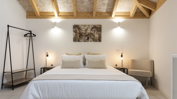 Une chambre avec un grand lit, deux tables de chevet avec des lampes, une chaise et un porte-vêtements suspendu.