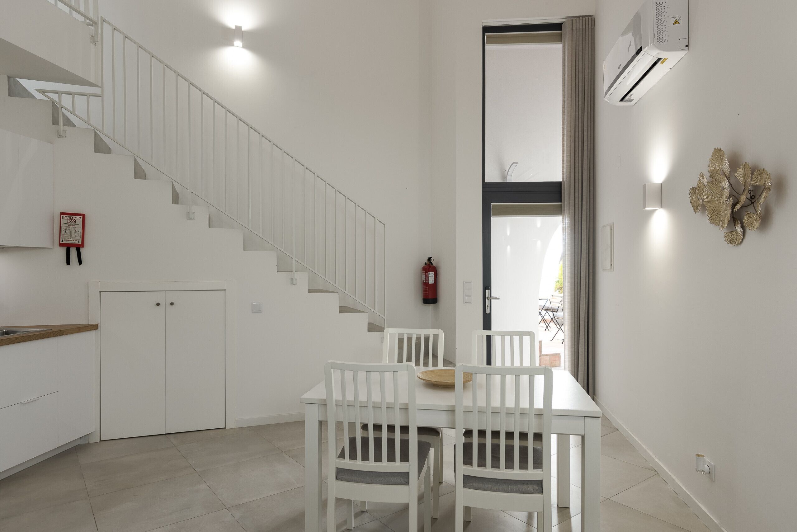 A modern kitchen with white cabinetry, a wooden countertop, and a dining area with white chairs and a table.