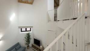Un vaste espace de vie doté d’un haut plafond, d’un escalier, d’un canapé, d’une télévision et d’une plante en pot.