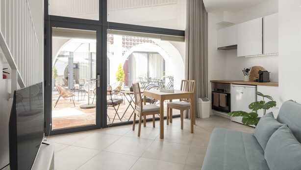 Een moderne woonkamer met een bank, een eettafel met stoelen en een keuken met kasten en apparatuur.