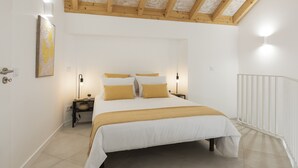 Een slaapkamer met een groot bed, twee nachtkastjes, een kunstwerk aan de muur en een witte leuning.