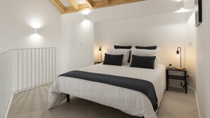 A bedroom with a large bed, white walls, wooden beams on the ceiling, and bedside lamps. - Madalena Village 2 - City centre by HD PROPERTIES (Faro)