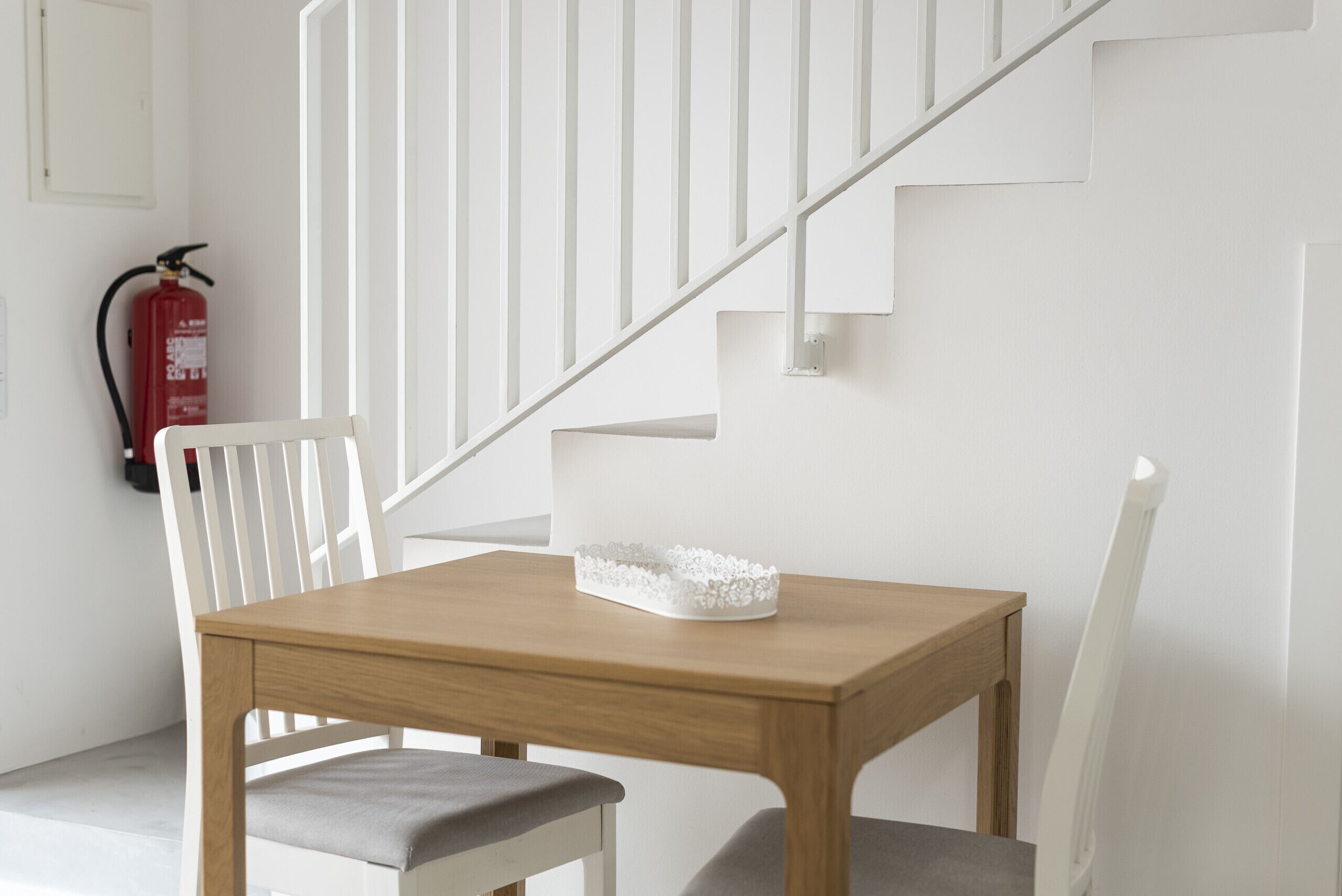 Una mesa de comedor de madera con una silla blanca, una escalera blanca y un extintor en la pared.