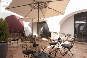 An outdoor patio with wooden tables and chairs, a large umbrella, and a potted plant.
