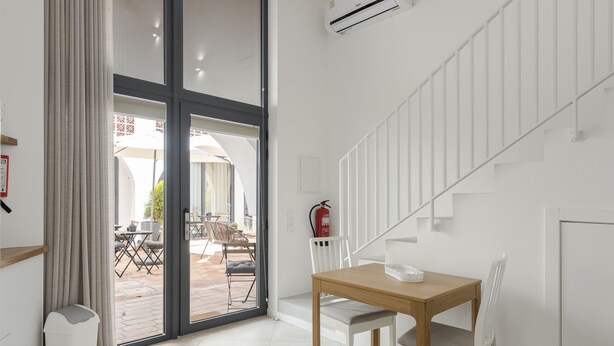 A modern room with a wooden table and chairs, a sliding glass door leading to an outdoor patio, and a white staircase. - Madalena Village 2 - City centre by HD PROPERTIES (Faro)